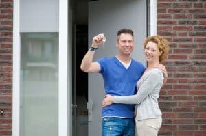 happy couple outside their house with keys to their home